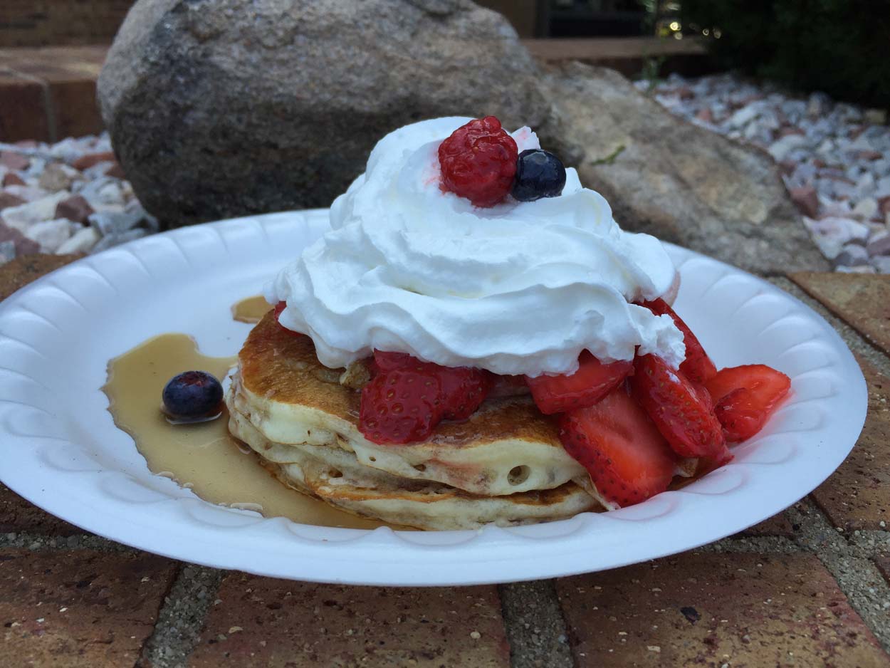 A white plate topped with pancakes and whipped cream.